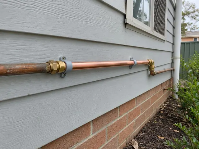 Repaired copper water pipe on an exterior weatherboard wall with brick base in Elermore Vale