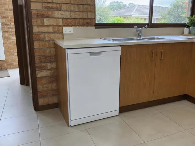 Built-in dishwasher beside a sink under a kitchen benchtop with brick wall and tiled floor in Glendale