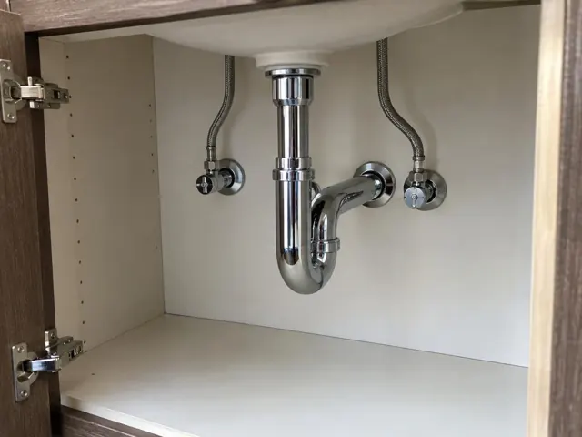 Neat under-sink plumbing with access panel and dry cabinet wall in Wallsend